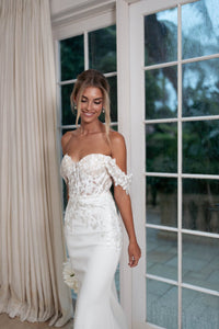 Ivory White Off The Shoulder Wedding Gown with Semi Sheer Corset Style Bodice, Sweetheart Off Shoulder Neckline, Lace Appliques, Fit and Flare Silhouette and Moderate Train