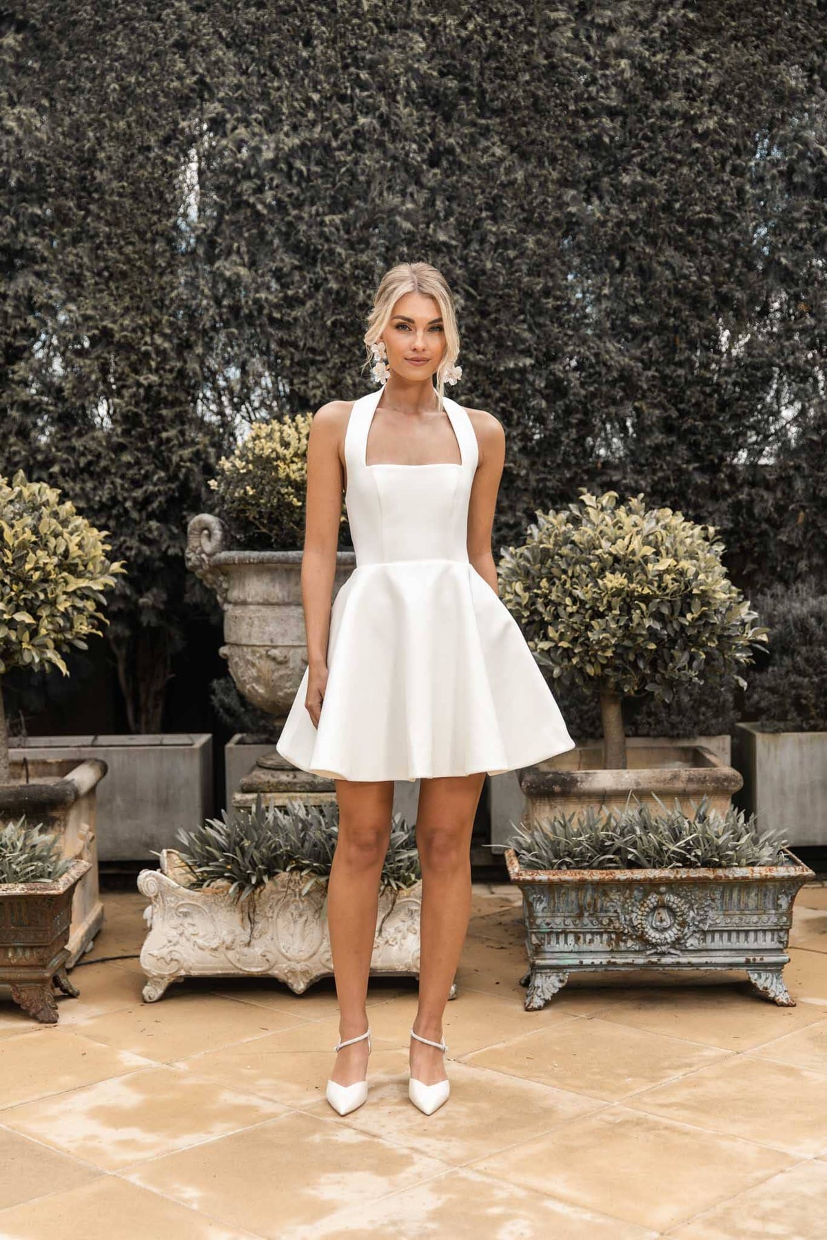 White Mini Dress with Wide Halter Straps and Structured Flared Mini Skirt worn with oversized floral earrings and white pumps